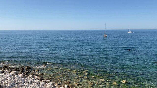 Majestic scenery with the Adriatic Sea in Portonovo and its finely rippling waters washing a shore of whitish rocks, a boat firmly above the water and other ones slowly skimming the surface of the sea