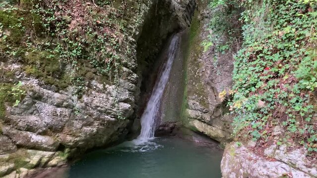 Firm view at Cascata del Pellegrino in Sarnano, a waterfall with a rushing stream of lush water flowing down in creamy colors, enclosed by majestic impenetrable stone, collecting in a calm basin below