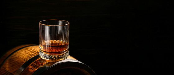 Glass of whiskey on wooden barrel against dark background with space for text