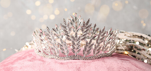 Beautiful tiara with dress on pink pillow against glowing lights. Prom concept