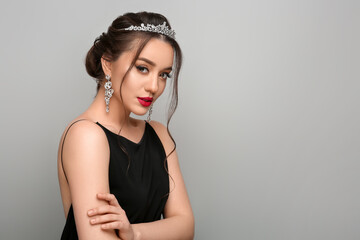 Beautiful young woman wearing luxurious tiara on light grey background, space for text