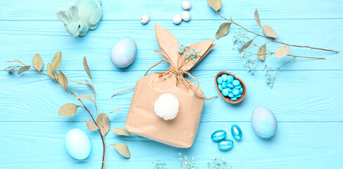 Composition with bunny gift bag, Easter eggs and floral decor on light blue wooden background