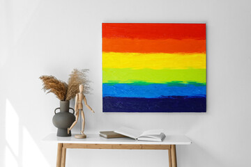 Table with vase, mannequin, books and painting of LGBT flag on light wall