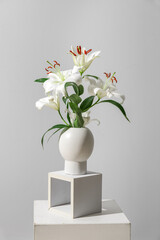 Vase with beautiful lilies on stand near grey wall