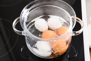 Fototapeta na wymiar Glass cooking pot with boiling eggs on stove in kitchen, closeup