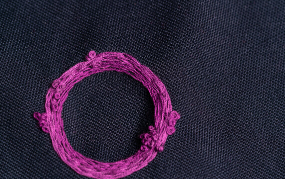 detalle de circulo fucsia bordado a mano sobre tela obscura