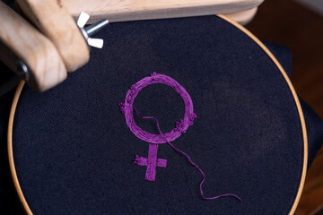 símbolo feminista bordado recién terminado con hilo suelto, sobre bastidor redondo de madera y...