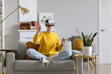 Pretty young woman in VR glasses sitting in sofa at home