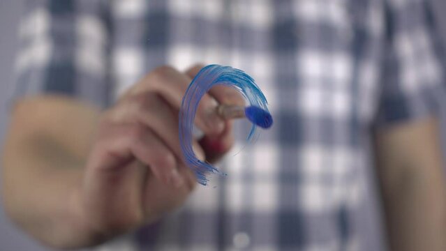 A man draws a male symbol on the glass. Sex symbol in blue is drawn with a brush. Close-up.