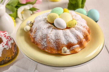 Dessert stand with tasty Easter cake and eggs on light wooden table, closeup