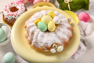 Dessert stand with tasty Easter cake and painted eggs on light wooden table, closeup