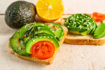 Delicious avocado toasts with sesame seeds and tomato on white wooden background