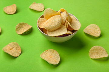 Bowl with delicious potato chips on green background