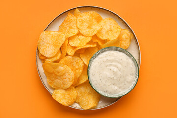 Plate with delicious potato chips and bowl of sauce on orange background