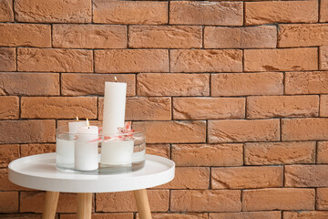 Burning candles on table near brown brick wall