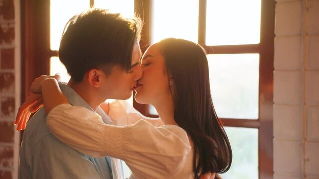 Asian young man and woman kissing each other in living room at home.