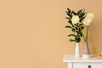 Vases with ranunculus flowers and plant branches on table near beige wall