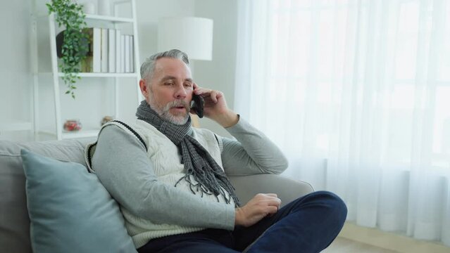 Caucasian senior elderly male using mobile phone in living room at home