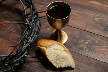 Crown of thorns with cup of wine and bread on wooden background, closeup