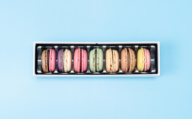Seven macaroons in a box on blue.
