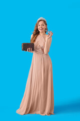 Fototapeta na wymiar Young woman in prom dress with purse and perfume on blue background