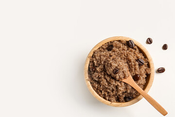 Bowl of body scrub and coffee beans on light background