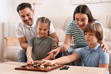 Fototapeta premium Parents playing checkers with children at table in room