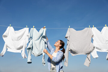 Woman hanging clothes with clothespins on washing line for drying against blue sky