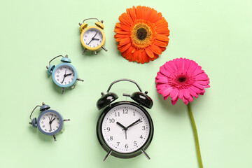 Alarm clocks and beautiful gerbera flowers on green background
