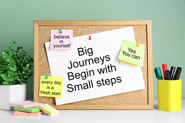 Corkboard with motivational quotes, potted houseplant and markers on white table