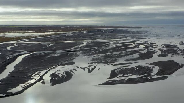 Aerial flyover river delta on Iceland during sunny and cloudy day - Ocean in background