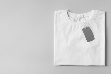 Stylish T-shirt with label on light grey background, top view. Space for text
