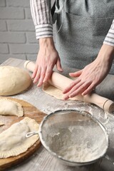 Woman rolling dough for chebureki at wooden table, closeup