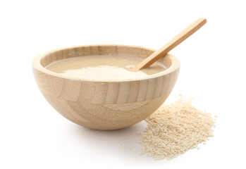 Wooden bowl with tasty tahini and sesame seeds on white background