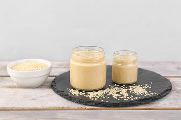 Slate board with jars of tasty tahini and sesame seeds on light wooden table
