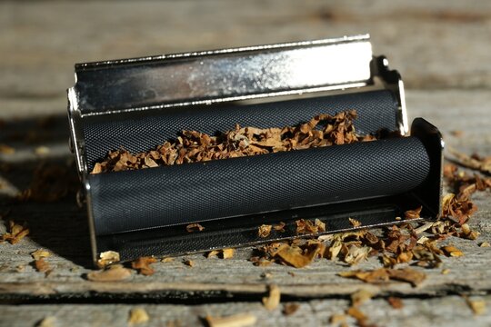 Roller with tobacco on old wooden table, closeup. Making hand rolled cigarettes