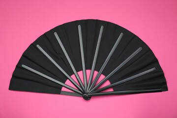 Stylish black hand fan on pink background, top view