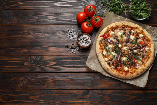 Tasty pizza with anchovies and ingredients on wooden table, flat lay. Space for text