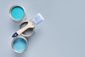 Cans with different paints and brush on light background, flat lay. Space for text