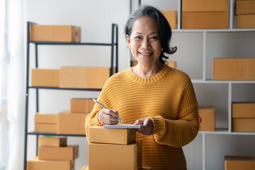 Fototapeta na wymiar Senior woman business owner selling online products, she is checking orders from customers, sending goods through a courier company, Senior woman concept opening an online store.