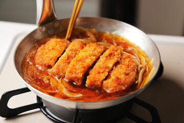 鍋で調理しているかつ丼
