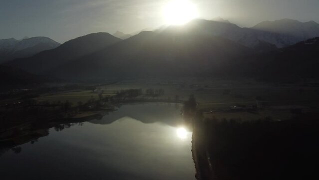 Aerial view from right to left over an alpine lake early in the morning. Sun shinning over the Mont Blanc, tallest mountain of Europe. Passy lake, Haute Savoie, France.