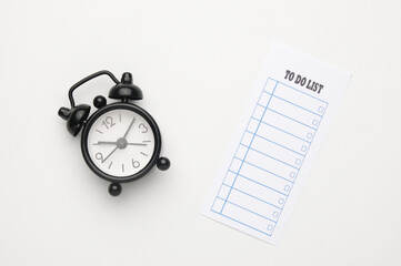 A picture of alarm clock and to do list on white background.