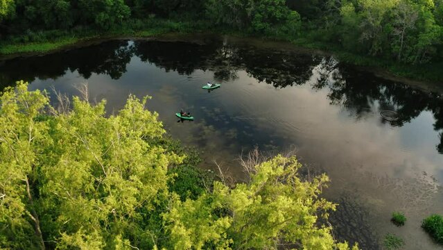 Aerial drone tilt down orbit over pair of kayaking fisherman on clear, still river water at sunrise