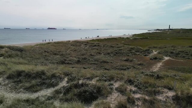 Aerial Orbit of Sand Dunes and Grass with Tourists on Beach and Ships on horizon, Skagen, Denmark