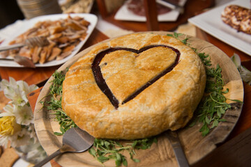 whole round baked brie on appetizer table with heart carved in the puffed pastry