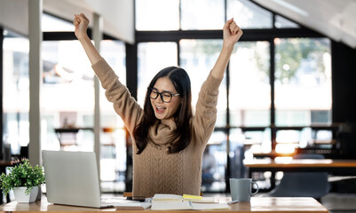 Elegant businesswoman sitting in office with digital tablet. Excited asian businesswoman raising hands to congratulate while working on laptop in office.