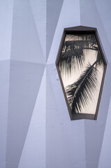 Two tone Gray Geometric Wall with a Polygon Gold Window Reflecting a Palm Tree.