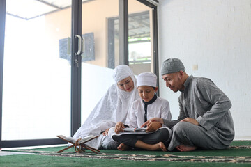 Muslim parents teach the children reading Quran, father pointing finger to Koran during a ramadan...
