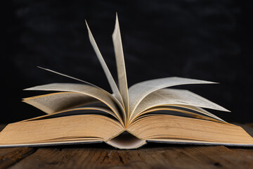 Open book of Bible on dark table. Low-key image of New Testament in bright light among darkness and shadows